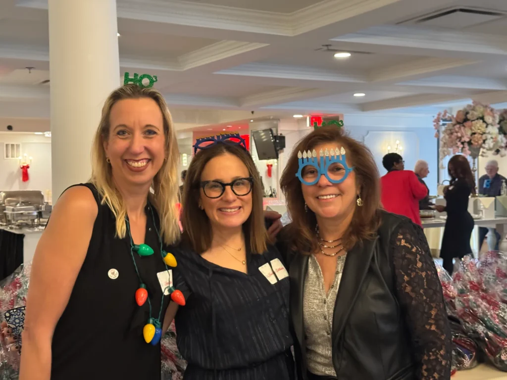 Three woman smiling while standing, wearing their festive glasses and headband